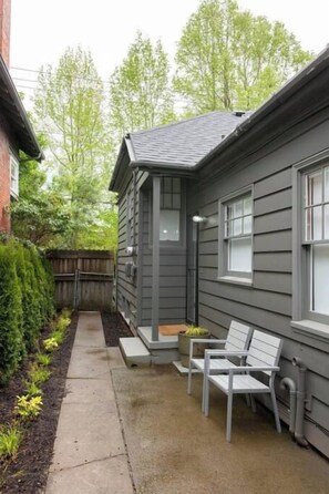 A small house with a covered porch, a concrete pathway, and a wooden fence.