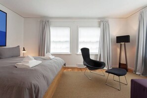 A hotel room with a bed, a chair, a standing lamp, and a window with curtains.