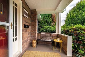 A covered porch with a brick wall, a bench, a small table, and a wicker basket.