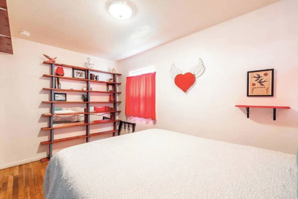 Une chambre à coucher avec un lit, une étagère en bois, un cœur rouge en guise de décoration et un tableau encadré accroché au mur.