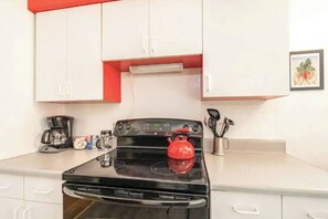 A kitchen with a black stove, white cabinets, and a red kettle.