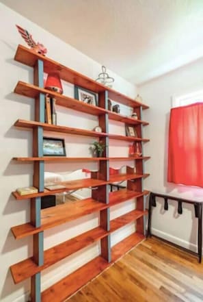A room with a wooden bookshelf against the wall, a small table with a chair, and a red curtain.
