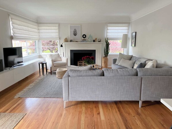 A living room with a grey sofa, a television, a fireplace, and a window with blinds.