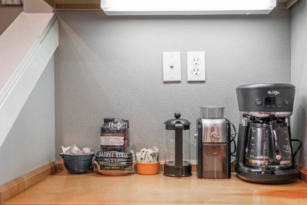 Une petite cuisine équipée d’une machine à café, d’un distributeur d’eau et d’un moulin à café, le tout posé sur le plan de travail.