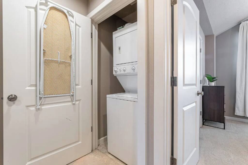 A laundry room with a washer and dryer, a door with a mesh screen, and a small cabinet with a plant.