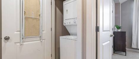 A laundry room with a washer and dryer, a door with a mesh screen, and a small cabinet with a plant.
