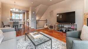 Un salon moderne avec un téléviseur à écran plat, une table basse et un canapé. Un escalier mène à un autre niveau, et il y a un coin repas avec des chaises et une table.