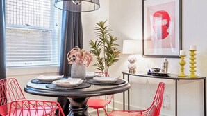 A dining area with a round table, red chairs, a potted plant, and a framed artwork on the wall. - The Braeburn: Luxury Flat, Steps From NW 23rd! (Portland)