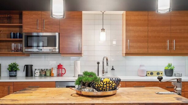 A modern kitchen with wooden cabinets, stainless steel appliances, and a central island with a bowl of lemons and a small tree. - The Braeburn: Luxury Flat, Steps From NW 23rd! (Portland)