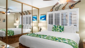 Une chambre avec un grand lit, un ventilateur de plafond, une fenêtre avec des volets et un miroir qui reflète la pièce.