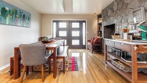 A dining area with a wooden table and chairs, a kitchen with stone backsplash, and a door leading to another room. - 4-bed home w GameRoom, FirePit & Saltwater Hot Tub (Vancouver)