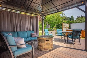 Une terrasse extérieure dotée d’un espace salon couvert, d’un foyer et d’une plateforme en bois.