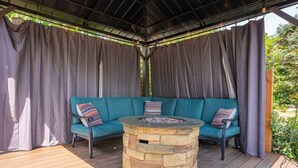 A covered outdoor seating area with a stone fire pit and teal cushioned seating. - 4-bed home w GameRoom, FirePit & Saltwater Hot Tub (Vancouver)