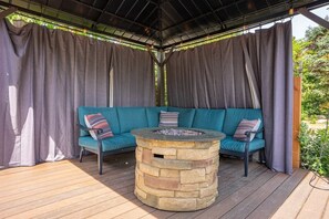 A covered outdoor seating area with a stone fire pit and teal cushioned seating. - 4-bed home w GameRoom, FirePit & Saltwater Hot Tub (Vancouver)