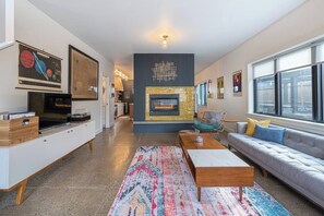 A modern living room with a fireplace, a sofa, a coffee table, and a television on a cabinet. - Bright and modern 2bd/2.5ba- close to Alberta st! (Portland)