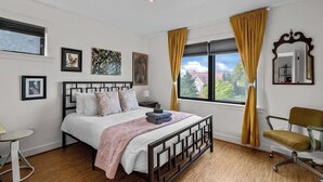 A bedroom with a bed, a chair, a desk, and a window with curtains.