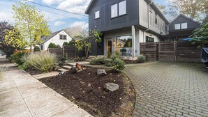 A two-story house with a dark exterior, a front porch, and a brick driveway. - Bright and modern 2bd/2.5ba- close to Alberta st! (Portland)
