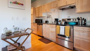 A modern kitchen with wooden cabinets, stainless steel appliances, and a dining area with a wooden table and chairs. - *On Alberta! Modern Artist Loft w/ Rooftop Views!* (Portland)