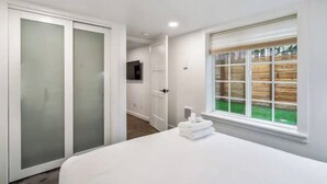 A bedroom with a large bed, a sliding door closet, a window with a view of a wooden fence, and a television on the wall.