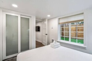 A bedroom with a large bed, a sliding door closet, a window with a view of a wooden fence, and a television on the wall.