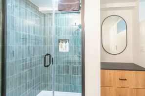 A bathroom with a glass shower enclosure, a wooden cabinet, and a round mirror on the wall. - 2 Bed/1 Bath in NE - Close to Mississippi Ave (Portland)