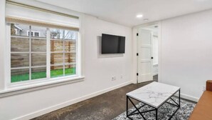 A modern room with a large window, a flat-screen TV mounted on the wall, and a marble-patterned coffee table. - 2 Bed/1 Bath in NE - Close to Mississippi Ave (Portland)