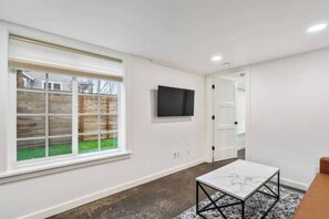 A modern room with a large window, a flat-screen TV mounted on the wall, and a marble-patterned coffee table.