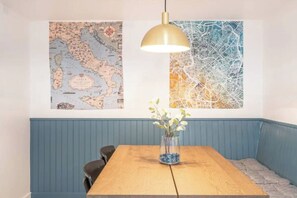 A dining area with a wooden table, a vase with flowers, and two maps on the wall.