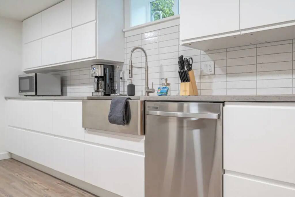 A modern kitchen with white cabinets, a stainless steel dishwasher, a microwave, and a coffee maker.