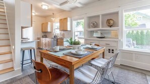 A modern kitchen with wooden cabinets, a dining table with chairs, and a large window with a view of greenery. - Modern, Sleek & Stylish: 2 blocks from Hawthorne! (Portland)