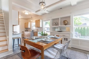 A modern kitchen with wooden cabinets, a dining table with chairs, and a large window with a view of greenery. - Modern, Sleek & Stylish: 2 blocks from Hawthorne! (Portland)