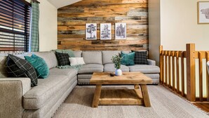 A living room with a wooden wall, a gray sectional sofa, a wooden coffee table, and a view of the outdoors.