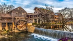 A historic mill with a large water wheel, wooden buildings, and a waterfall.