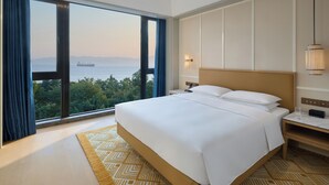 Habitación de hotel con una cama grande, una mesita de noche, una lámpara y vistas al mar a través de amplios ventanales.