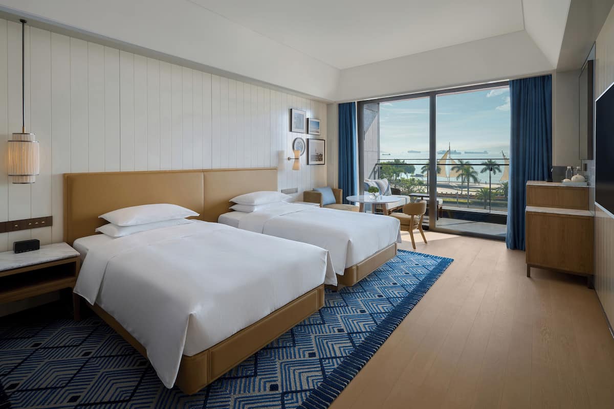 Habitación de hotel con dos camas, un balcón con vistas, una mesita y un televisor.