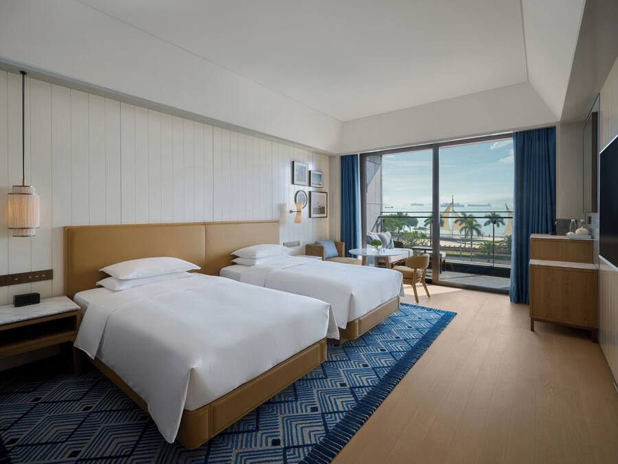 Ein Hotelzimmer mit zwei Betten, einem Balkon mit Blick, einem kleinen Tisch und einem Fernseher.