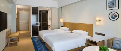 A hotel room with two beds, a desk, a chair, a TV, and a small table with a plant.