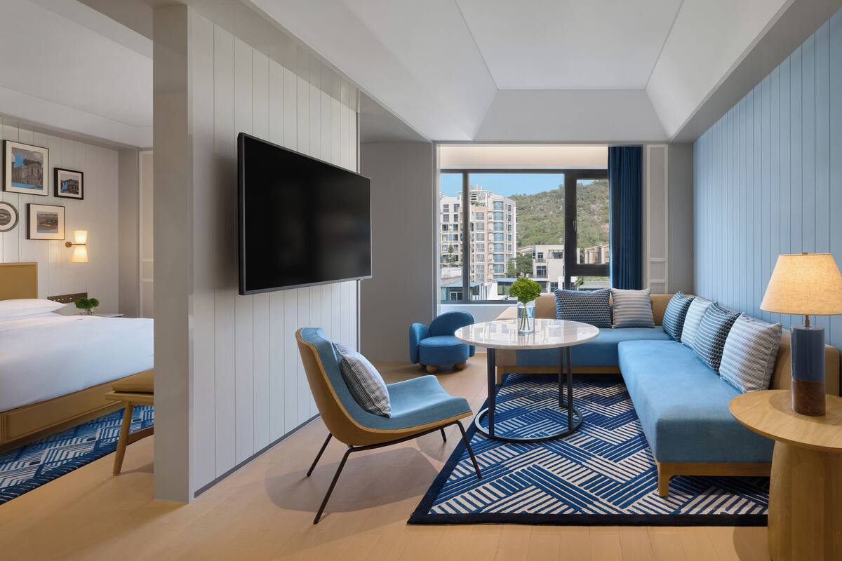 Una habitación de hotel moderna con cama, televisión, sofá, mesa de centro y vista a edificios.
