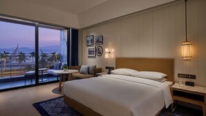 Un hotel moderno con una cama grande, un balcón con vista a la playa y una pequeña zona de estar con una mesa.