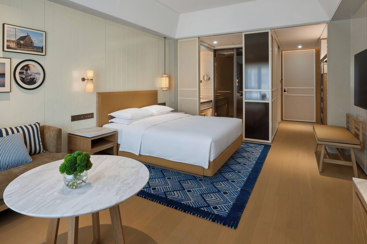 Una habitación de hotel con una cama, un sofá, una mesita con un florero y un televisor.