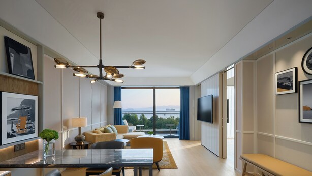 Habitación de hotel moderna con comedor, un sofá, televisor montado en la pared y vistas a la ciudad.