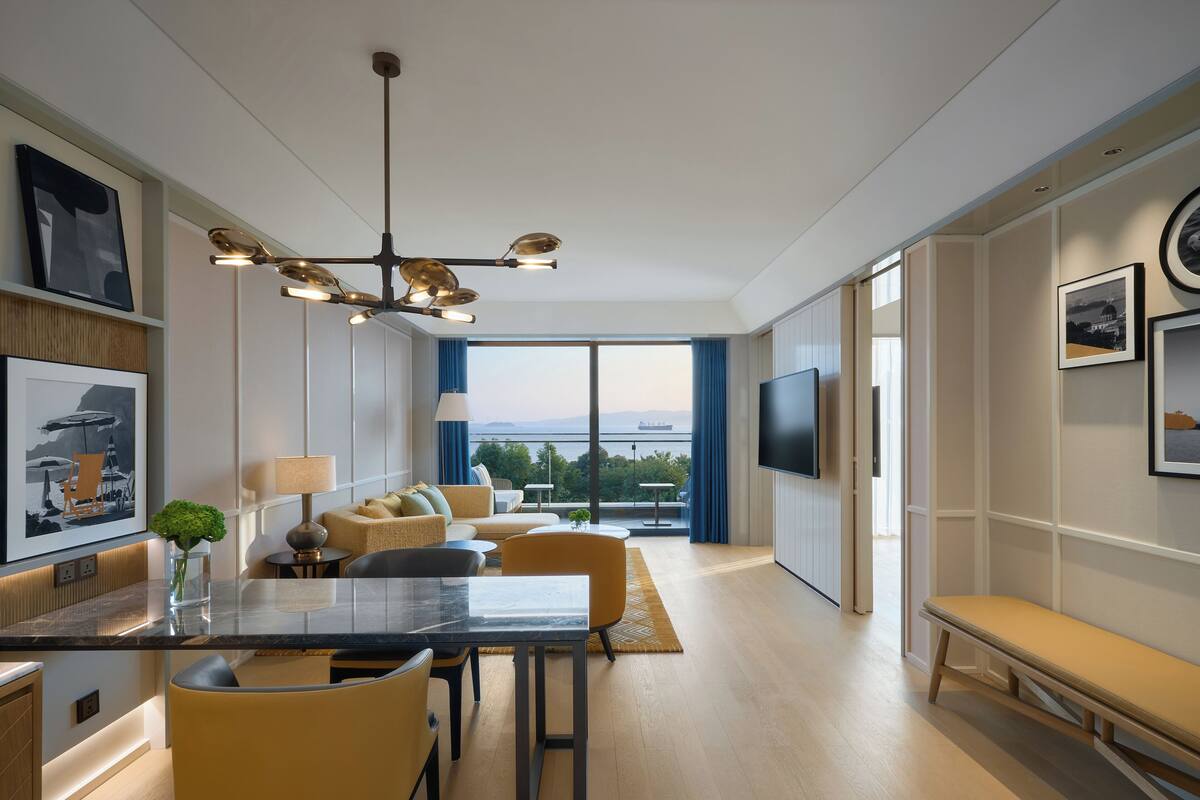 Habitación de hotel moderna con comedor, un sofá, televisor montado en la pared y vistas a la ciudad.