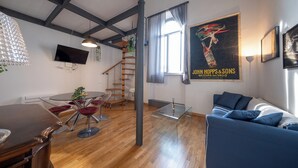 Ein modernes Wohnzimmer mit Holzboden, einem blauen Sofa, einem Glastisch und einem an der Wand befestigten Fernseher.