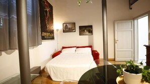 Ein Schlafzimmer mit einem Bett, einem roten Sofa, einem Glastisch und einer Topfpflanze.