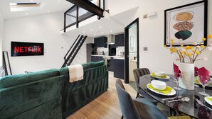 A modern living space with a green sofa, a dining table set with plates and glasses, and a staircase leading to an upper level. - Elegant Yorkshire Abode - Great Location - Sleeps 19 (Castleford)