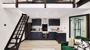 A modern kitchen with dark cabinets, a stainless steel range hood, and a built-in oven. A wooden ladder leads to a lofted area above. - Elegant Yorkshire Abode - Great Location - Sleeps 19 (Castleford)