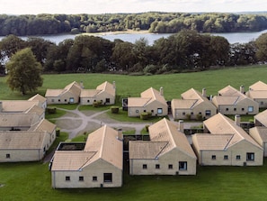 A cluster of uniform, single-story buildings with pitched roofs, surrounded by a well-maintained lawn and a body of water in the background. - 6 Person Holiday Park Home in Middelfart (Middelfart)