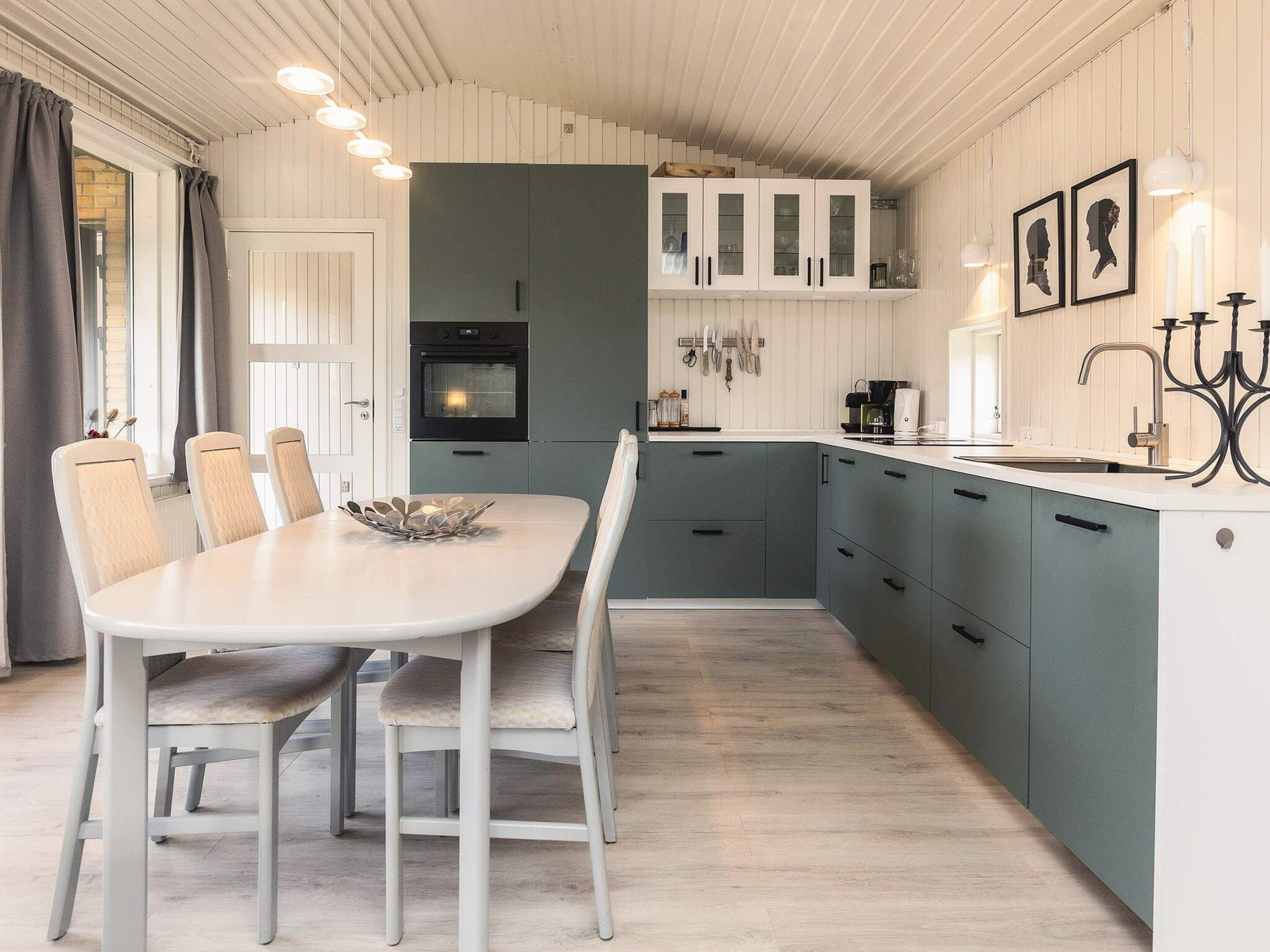 A modern kitchen with a dining area, featuring a white table, grey cabinets, and a built-in oven.