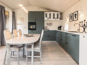 A modern kitchen with a dining area, featuring a white table, grey cabinets, and a built-in oven.