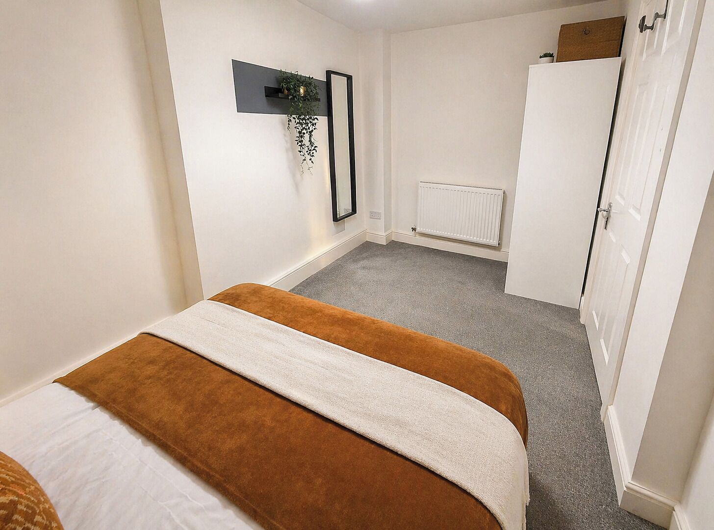 Un dormitorio con cama, radiador, armario y estante de pared con una planta.